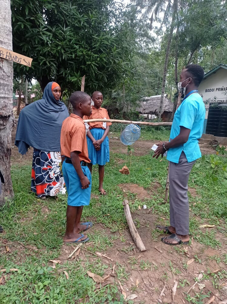 Student helps pupils to build a tippy tap installation for hand washing at the primary school in Bodoi. Photo: © Rebekah Makau